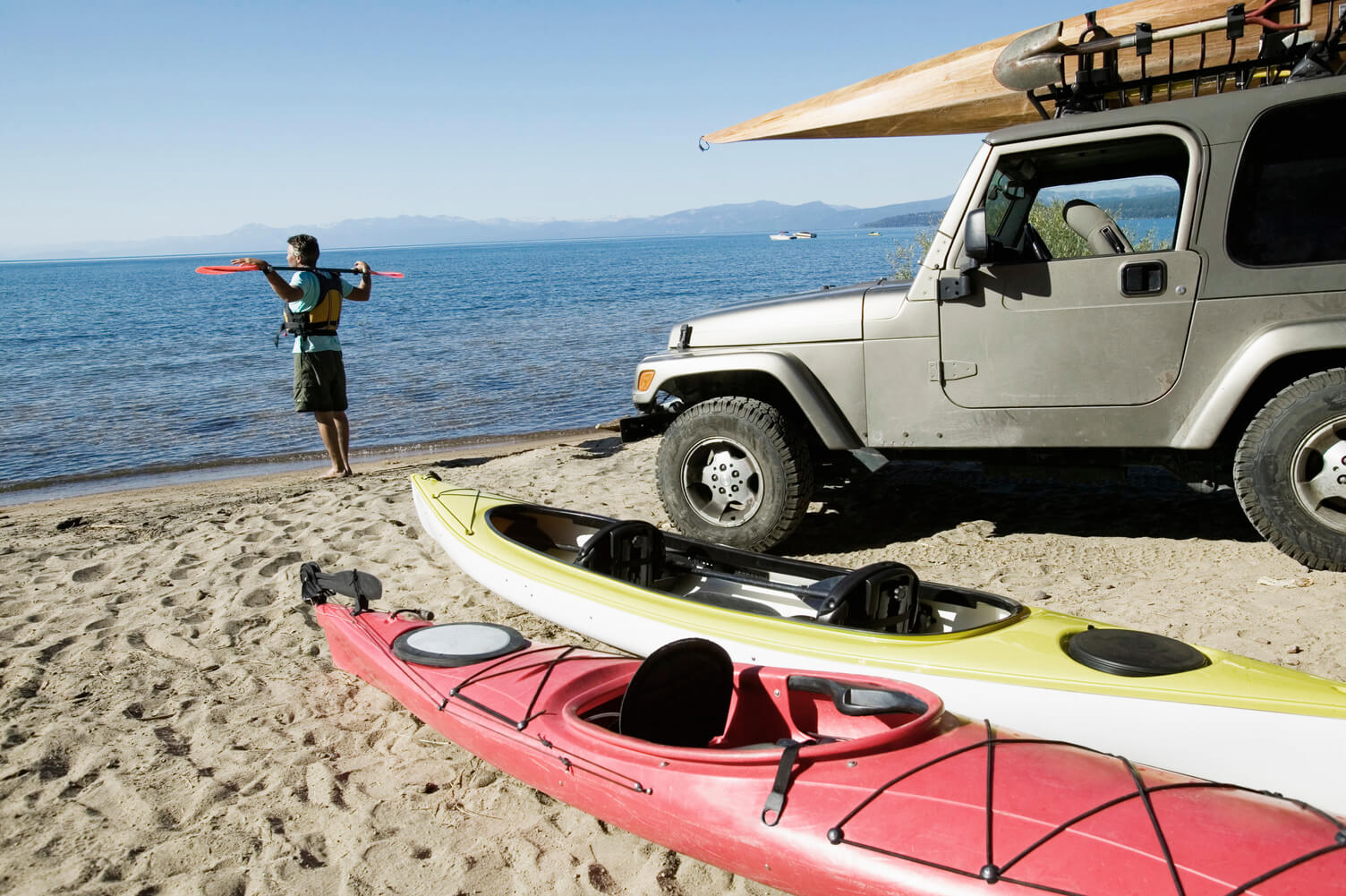 Kayaker looking towards the ocean with kayaks and utility vehicle behind him on the beach.