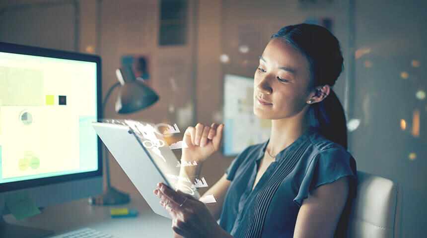 Young asian woman sitting in front of her computer and laptop, with technological graphics popping out toward her.